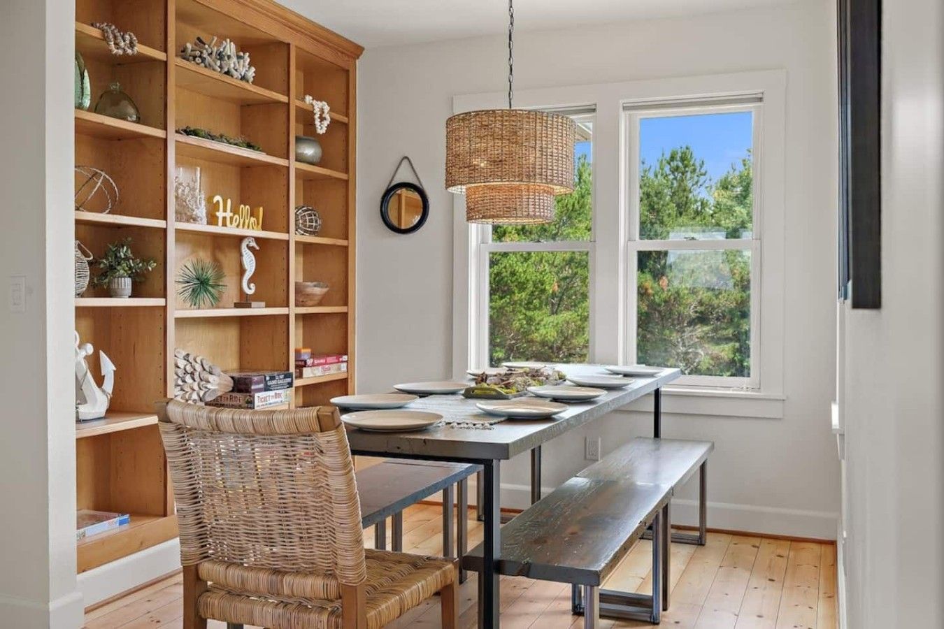 A dining area with a wooden bookshelf, wicker chair, and a hanging light fixture.