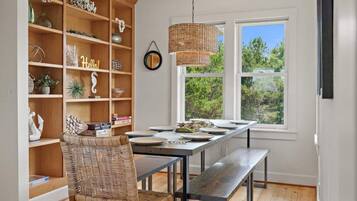 A dining area with a wooden bookshelf, wicker chair, and a hanging light fixture.