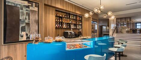 A modern bar area with a blue counter, bar stools, a coffee machine, and a variety of liquor bottles.