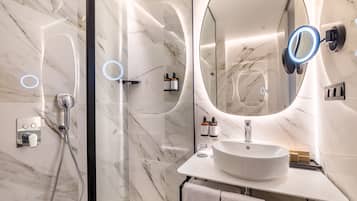 A modern bathroom with a marble floor, a round sink, a large mirror with a light, and a handheld showerhead.