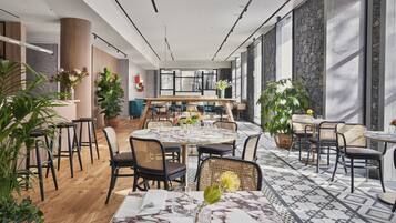 A modern dining area with round tables, wicker chairs, and potted plants.