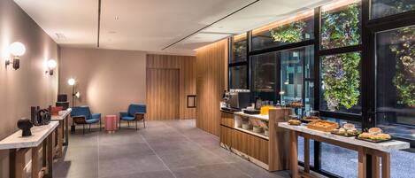 A modern hotel lobby with a long reception desk, seating area, and a large window with a view of greenery.