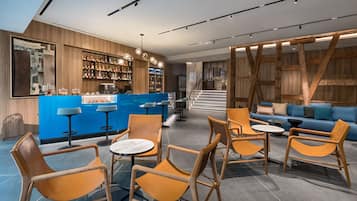 Una zona de bar moderna con un mostrador azul, estantes de madera con botellas y sillas naranjas alrededor de mesas.