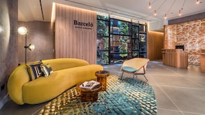 A modern hotel lobby with a yellow sofa, a wooden reception desk, and a large window with a view of greenery. - Barcelo Funchal Oldtown (Funchal)