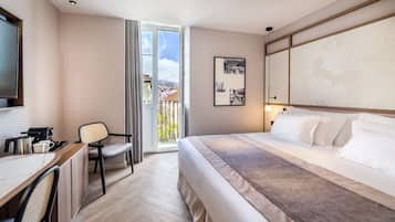 Ein Hotelzimmer mit Bett, Schreibtisch mit Stuhl, Fernseher und einem Balkon mit Stadtblick.
