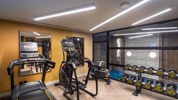 Un gimnasio moderno con máquinas de cardio, un espejo grande y un estante con mancuernas.