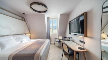 A modern hotel room with a large bed, a desk with a flat-screen TV, a coffee maker, and a large window with a view.