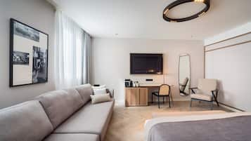 Una habitación de hotel moderna con sofá, escritorio, silla, cama, televisor y espejo.
