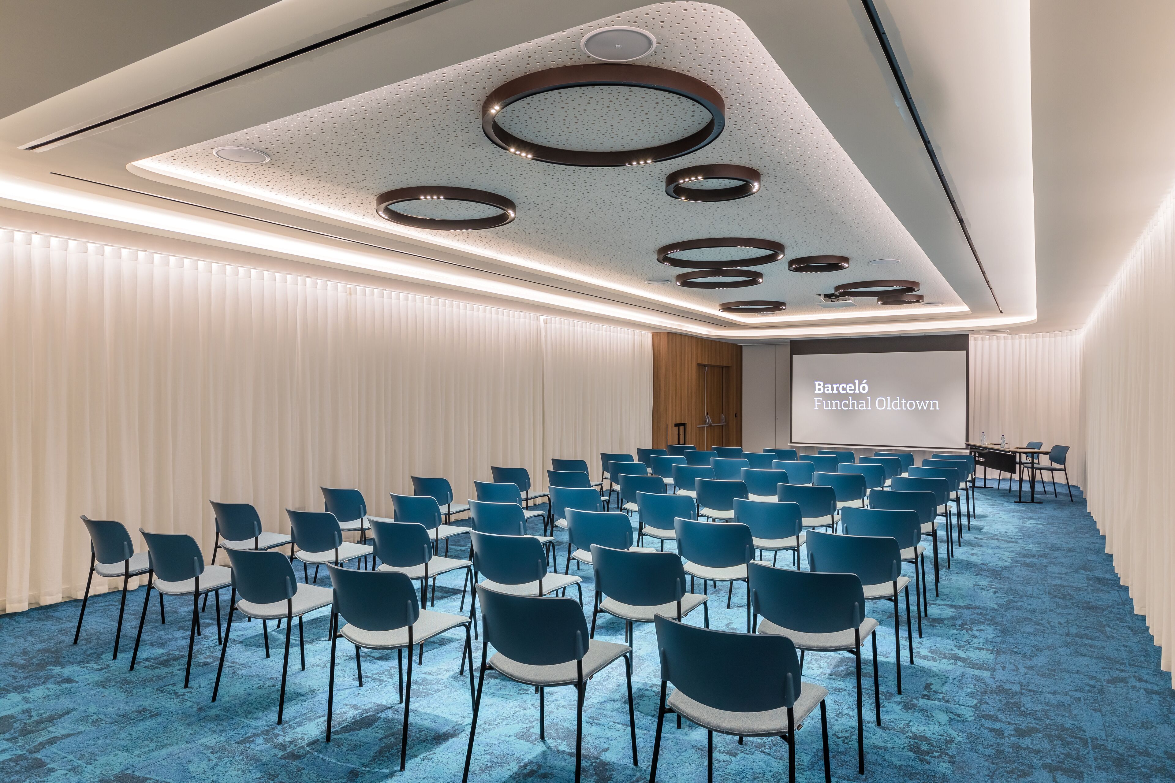 A conference room with rows of chairs, a projector screen, and a modern ceiling design.