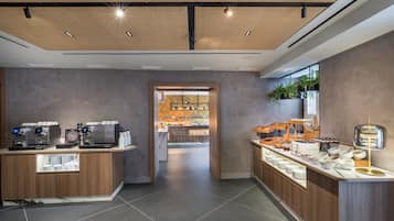 A modern cafe with a wooden counter, coffee machines, and a variety of food items.