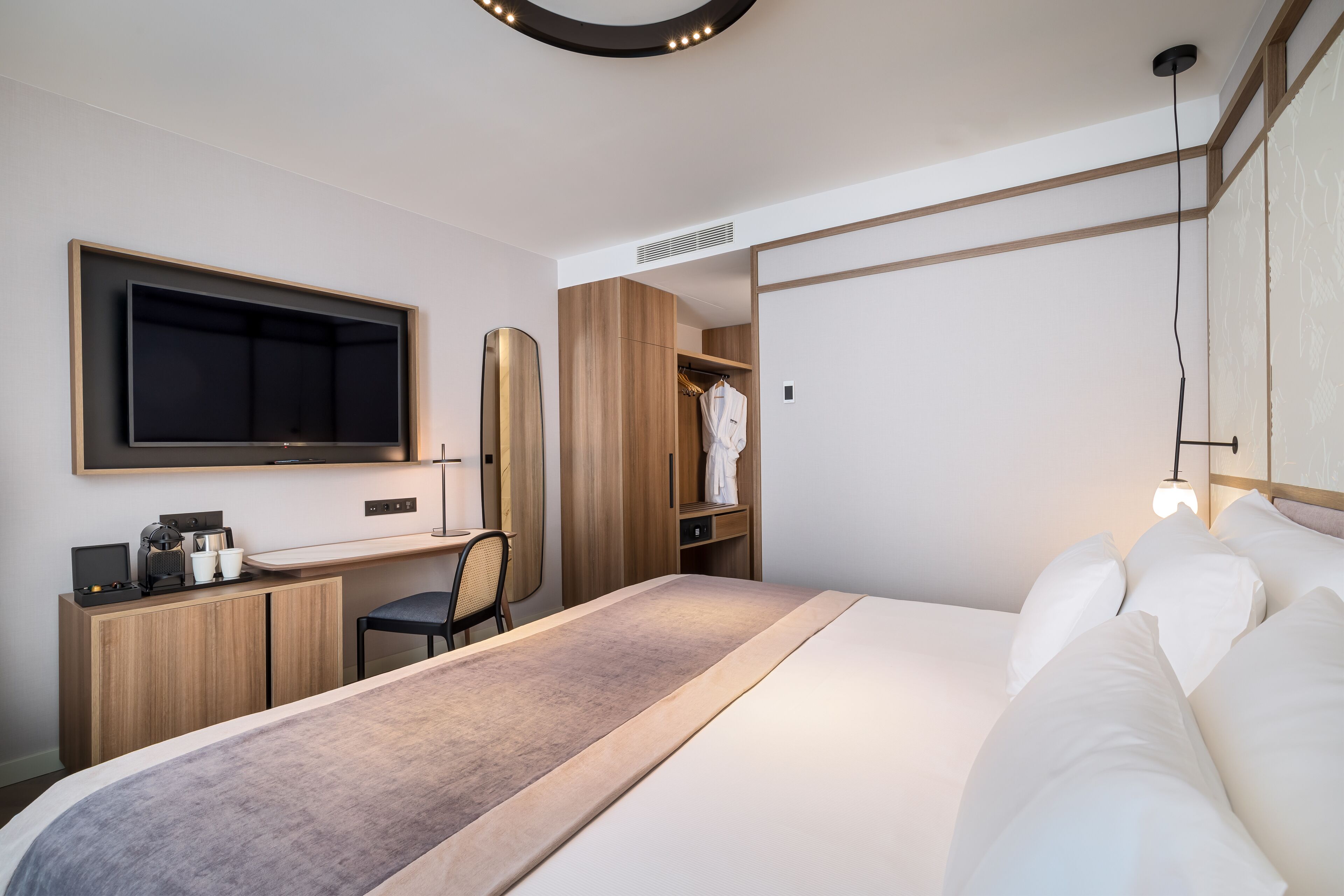 Una habitación de hotel moderna con una cama grande, un escritorio con silla, un armario y un televisor montado en la pared.