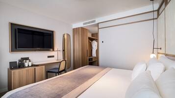 Una habitación de hotel moderna con una cama grande, un escritorio con silla, un armario y un televisor montado en la pared.