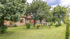 Ein Steinhaus mit gepflegtem Rasen, einem kleinen Baum und einem roten Auto im Hintergrund.