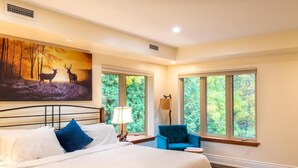 A bedroom with a large bed, two bedside lamps, a blue chair, and a painting of deer on the wall. - Fairy Bay Lakehouse (Huntsville)
