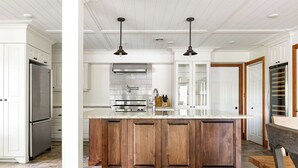 A kitchen with a large wooden island, white cabinetry, stainless steel appliances, and pendant lighting. - Fairy Bay Lakehouse (Huntsville)