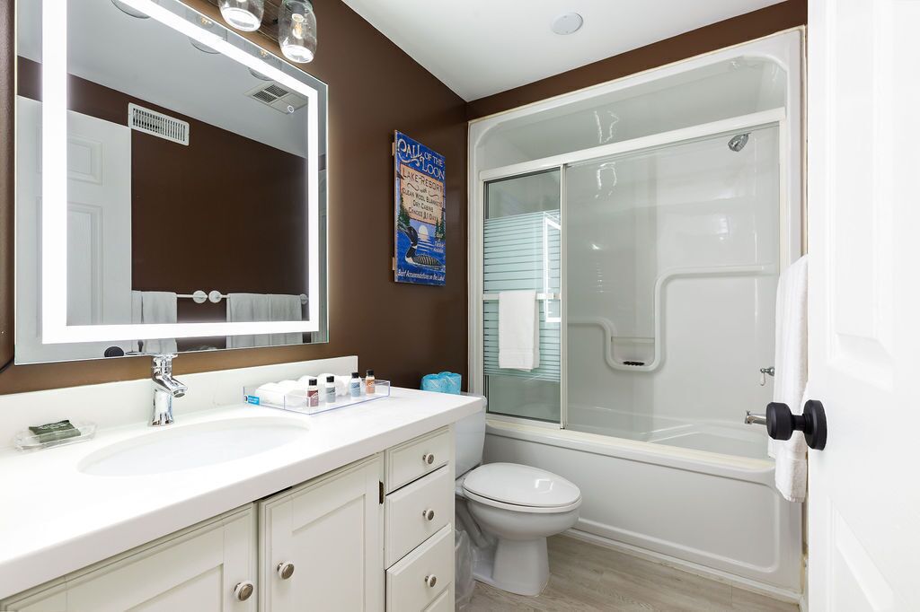 A bathroom with a white sink, a large mirror, a toilet, and a glass-enclosed shower.