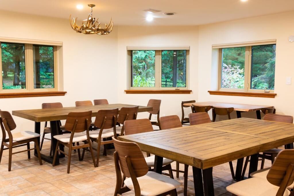 A dining area with wooden tables and chairs, large windows with forest views, and a chandelier.