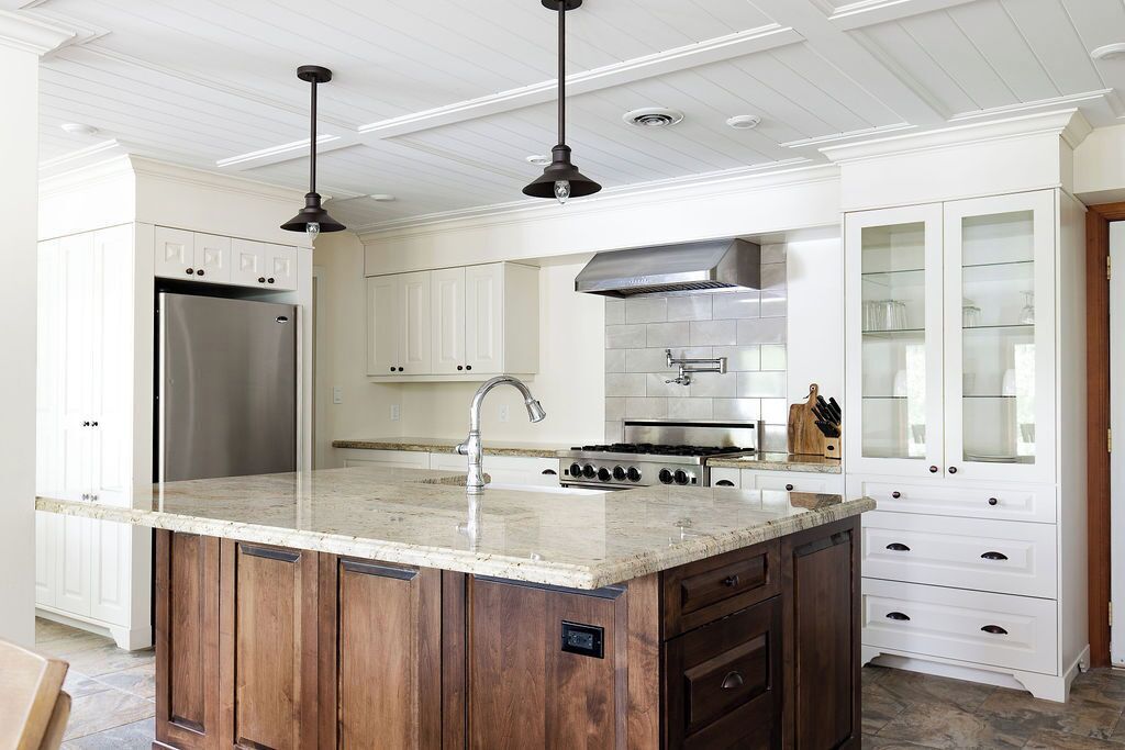A modern kitchen with white cabinetry, a stainless steel refrigerator, a central island with a sink, and a gas stove.