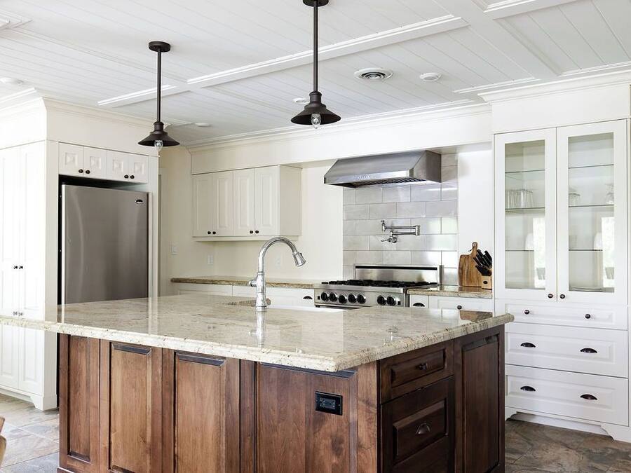 A modern kitchen with white cabinetry, a stainless steel refrigerator, a central island with a sink, and a gas stove.