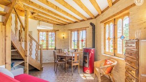 Una habitación acogedora con una escalera de madera, una mesa de comedor con sillas, una chimenea roja y un sillón de mimbre con cojín.