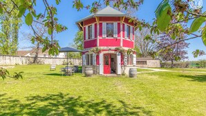 Una estructura en forma de torre de color rojo y blanco, con una puerta y ventanas, rodeada por un área de césped y árboles.