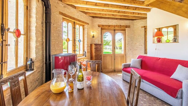 Un interior rústico con vigas de madera a la vista, una mesa de madera con vasos y botellas, un sofá rojo y una chimenea.