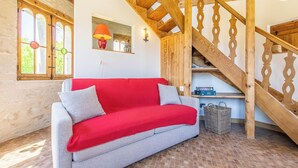 Una habitación acogedora con un sofá rojo, una escalera de madera y un suelo de ladrillo.