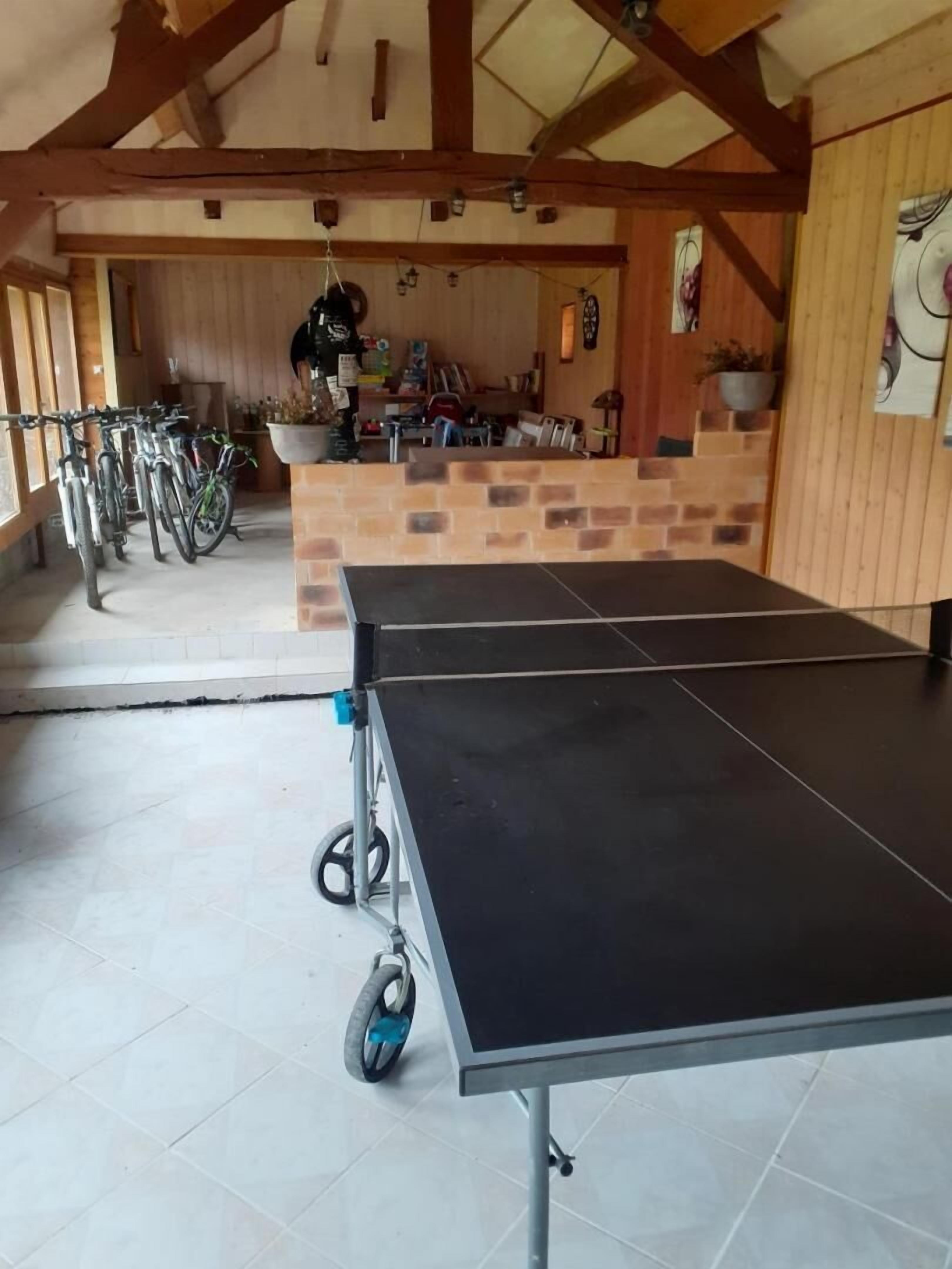 A ping pong table in a room with a tiled floor and wooden beams on the ceiling.