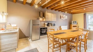 Una cocina moderna con vigas de madera, un comedor con mesa y sillas de madera, y un televisor pequeño sobre un mueble de madera.