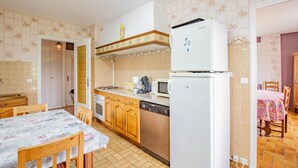 A compact kitchen with a refrigerator, microwave, stove, and dishwasher. There is a dining table with chairs and a patterned tablecloth. The kitchen has wooden cabinets and a tiled backsplash. - Le Champ des Charmes (SAINT-DIDIER-SUR-ARROUX)