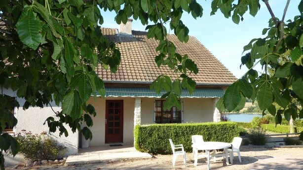 A house with a tiled roof, a front door, and a small patio with chairs and a table. - Le Champ des Charmes (SAINT-DIDIER-SUR-ARROUX)