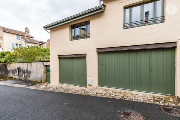 A two-story building with a beige facade, two green double garage doors, and a small balcony with a metal railing. - la Maison Dalice - Cluny (CLUNY)