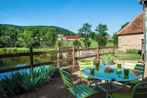 A patio with a table and chairs, a wooden fence, and a pond. - Le Moulin - DYO - Gîte (DYO)