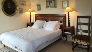A neatly made bed with white linens, two bedside lamps, a wooden headboard, and a chair with a striped cushion.