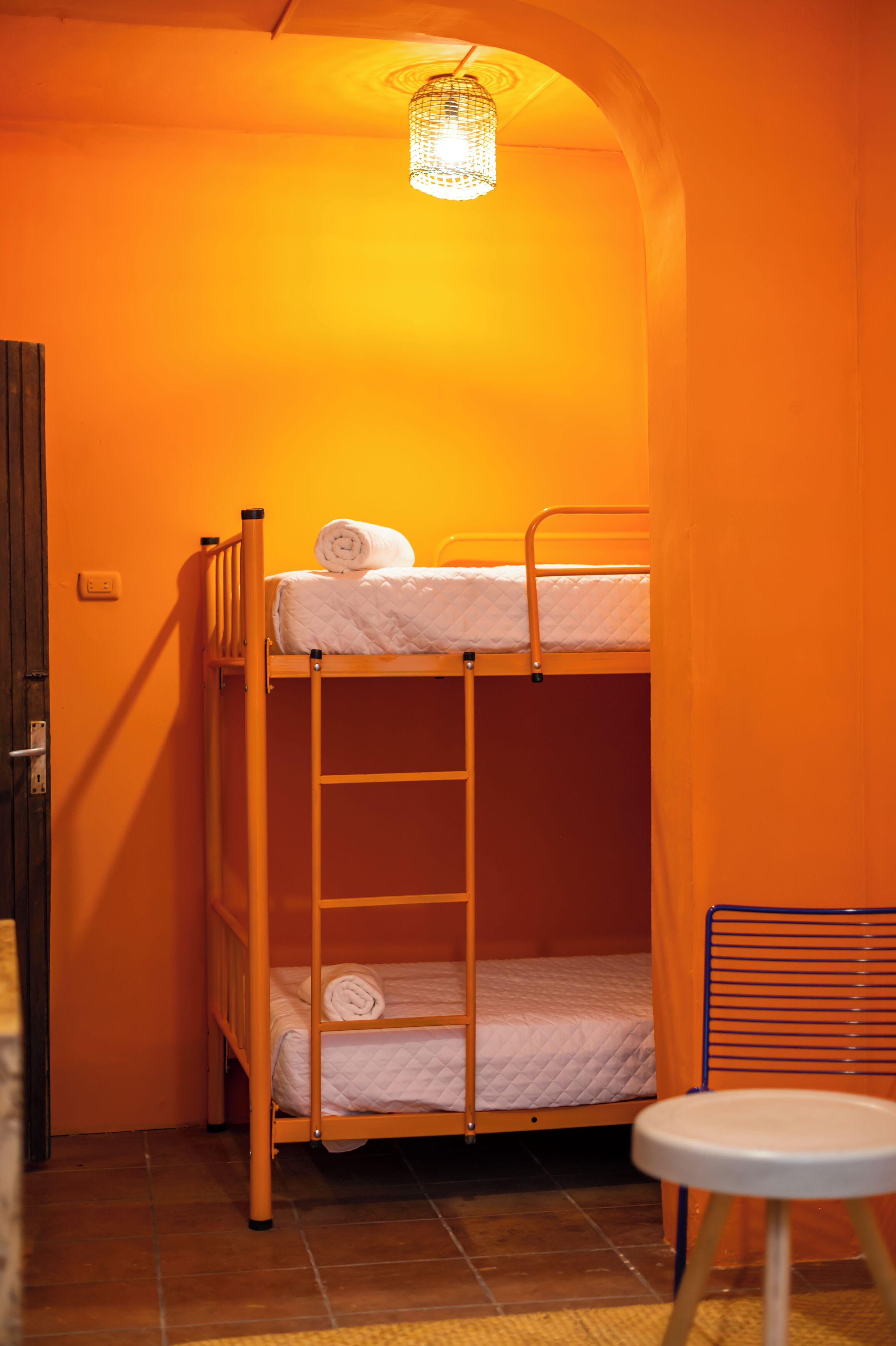 A bunk bed with a ladder, a small table, and a hanging light fixture in a room with orange walls.