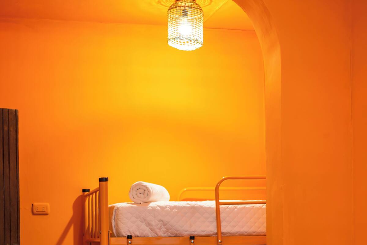 A bunk bed with a ladder, a small table, and a hanging light fixture in a room with orange walls.