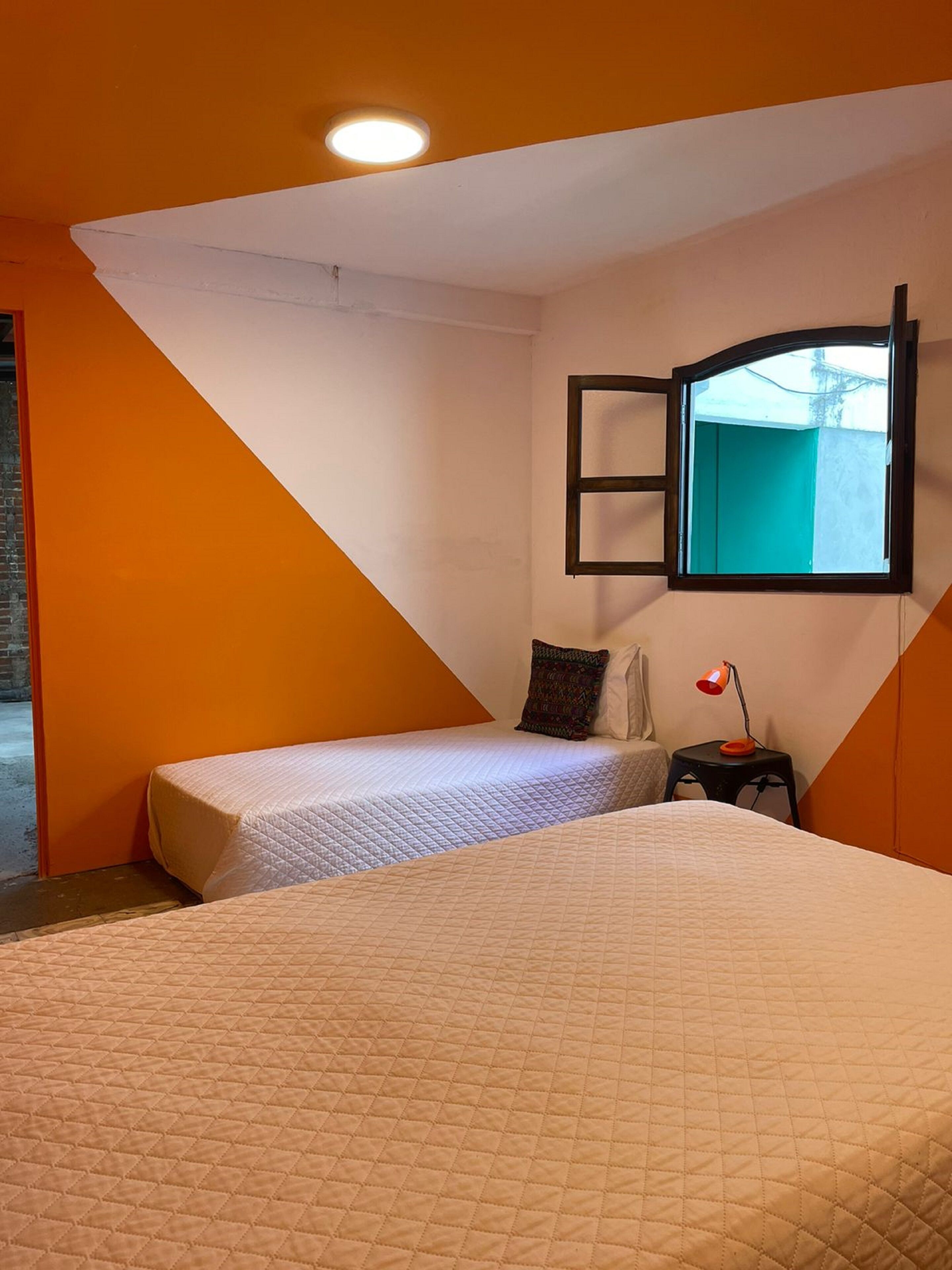 A bedroom with two beds, a small table with a lamp, and a window with a view of the outside.