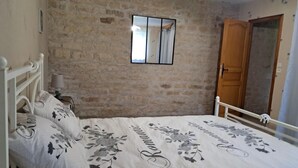 A bedroom with a stone wall, a bed with floral bedding, a bedside lamp, and a wooden wardrobe. - Le Charneron - Chardonnay (CHARDONNAY)