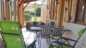 A covered patio with outdoor furniture, including chairs and a table, surrounded by greenery. - Le Charneron - Chardonnay (CHARDONNAY)