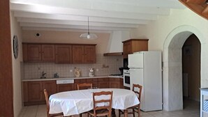 A kitchen with wooden cabinets, a white refrigerator, a dining table with chairs, and a hanging light fixture. - Le Charneron - Chardonnay (CHARDONNAY)