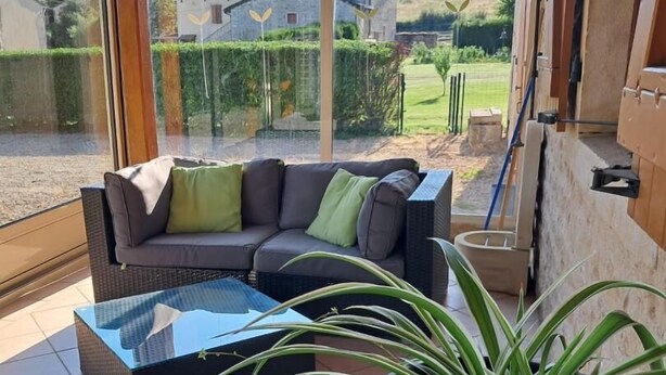 A covered patio with a sofa and a glass coffee table, a potted plant, and a view of houses and greenery. - Le Charneron - Chardonnay (CHARDONNAY)