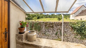 A covered outdoor area with a stone wall, a wooden door, and a potted plant. - Le Verger - Paris L'hopital (PARIS L'HOPITAL)