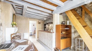 A rustic interior with exposed wooden beams, a wooden staircase, a kitchen area, and a dining table with documents. - Le Verger - Paris L'hopital (PARIS L'HOPITAL)