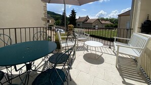 Un patio con una mesa y sillas, una sombrilla y vistas a casas y follaje.