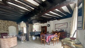 Una habitación amplia con suelo de baldosas hexagonales, una mesa de madera con sillas, un sofá, una pared de piedra y un techo con vigas a la vista.