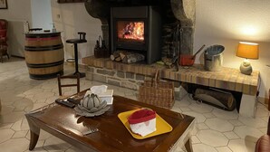 Una sala de estar acogedora con chimenea de piedra, un barril de madera, una mesa con un objeto decorativo y una lámpara.