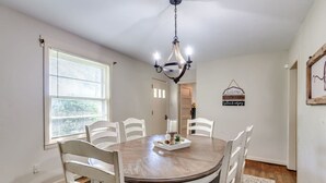 A dining room with a round table, white chairs, a chandelier, and a window with blinds. - Calm Country Oasis - Creek, ATV Trls & Norris Lake (Speedwell)
