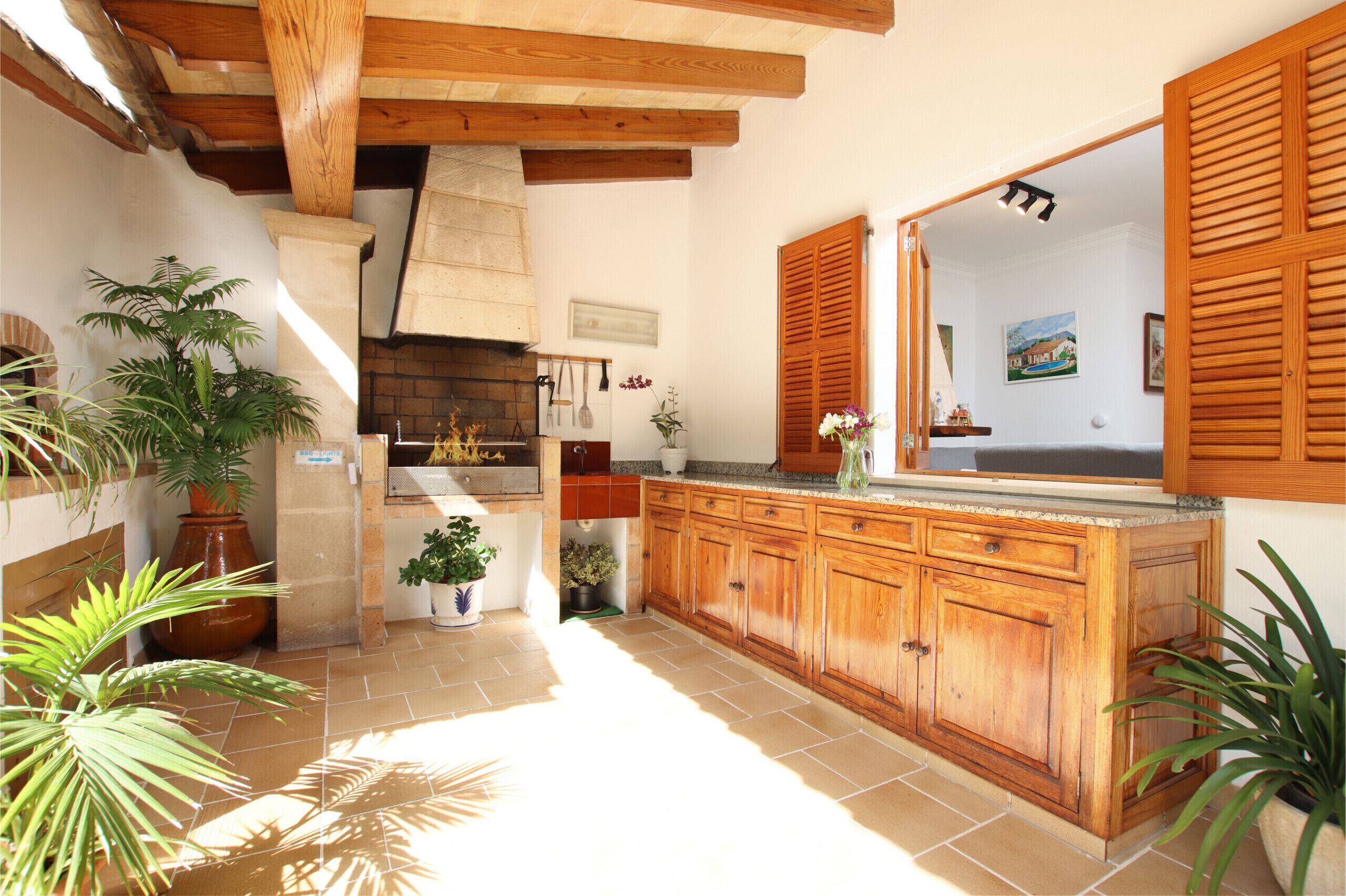 Cocina con armarios de madera, suelo de baldosas y plantas en macetas.