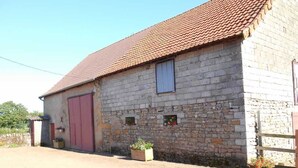 Un bâtiment en pierre avec un toit recouvert de tuiles rouges, une porte rouge et de petites fenêtres.