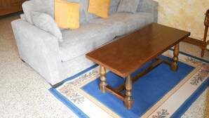 Un salon avec un canapé gris, deux coussins jaunes, une table basse en bois et un tapis à motifs.